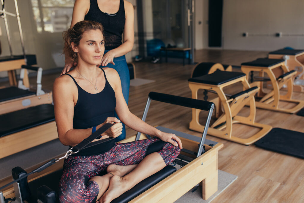 A pilates instructor providing guidance to a woman on a pilates reformer